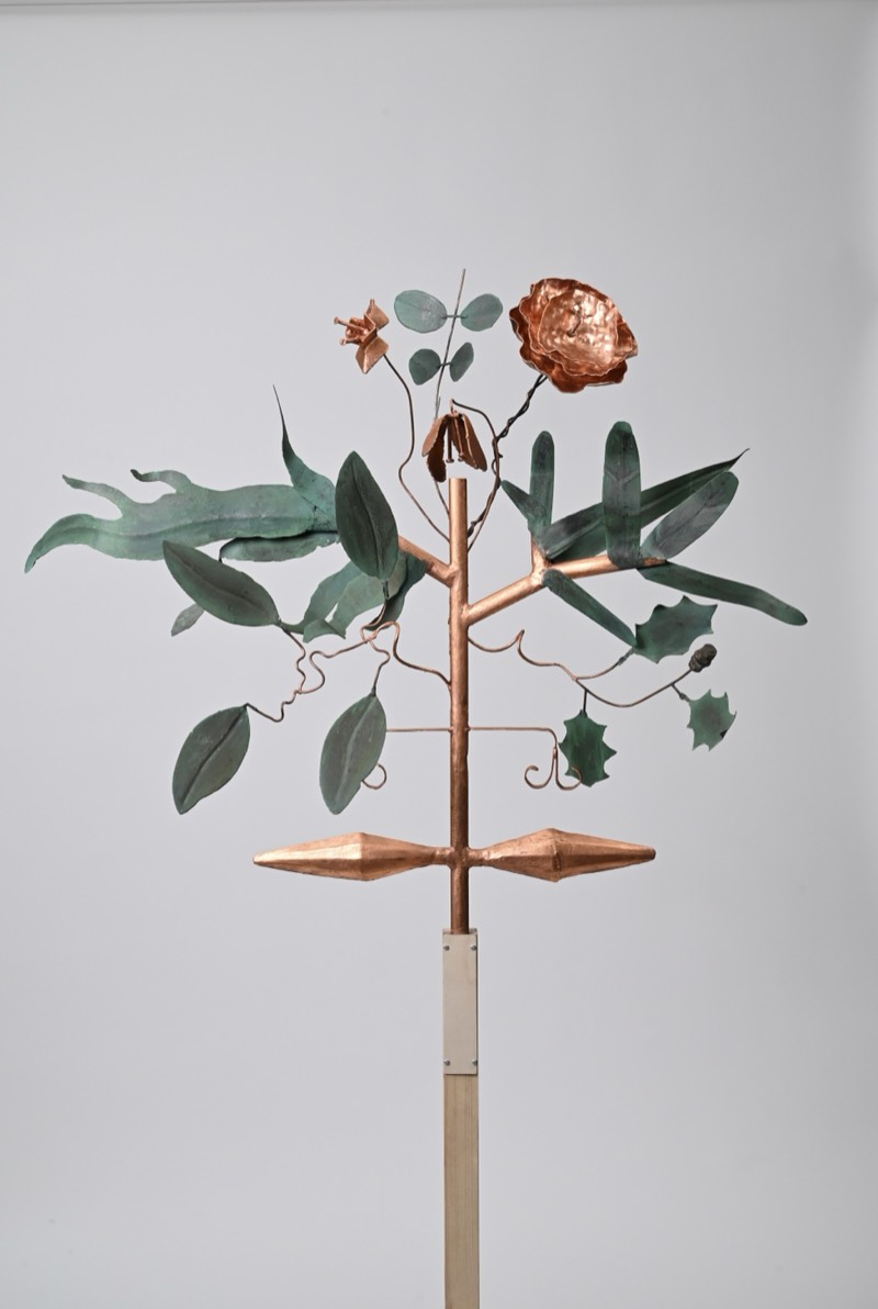 Full view of a copper plant sculpture with patinated verdigris leaves and a copper bloom on a central stem.