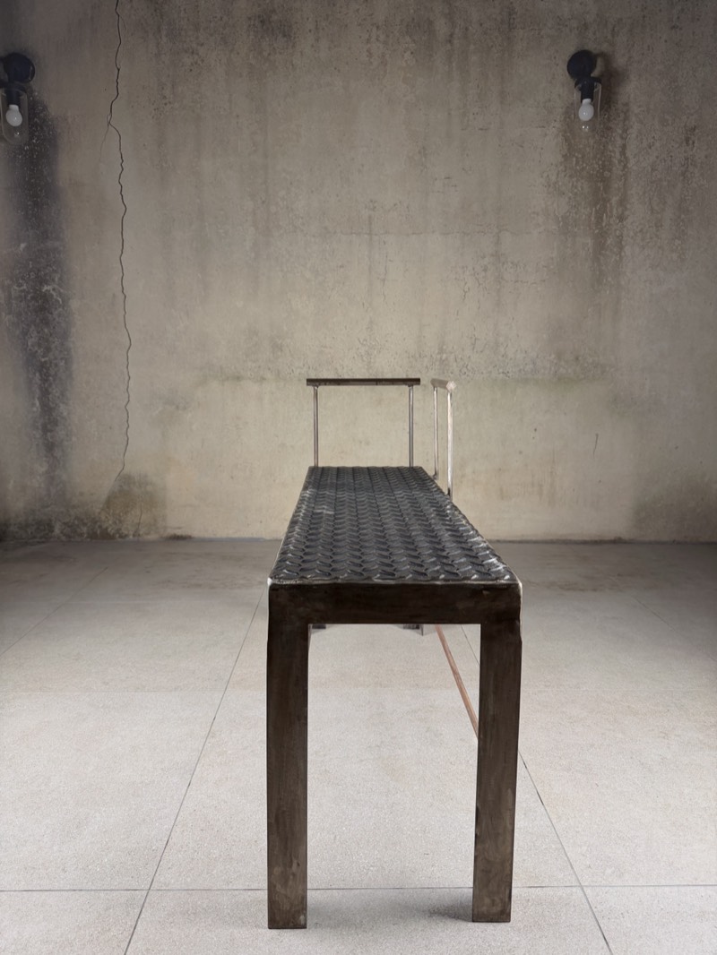 Long profile of the raw steel bench, seat and rail running the length of the frame.